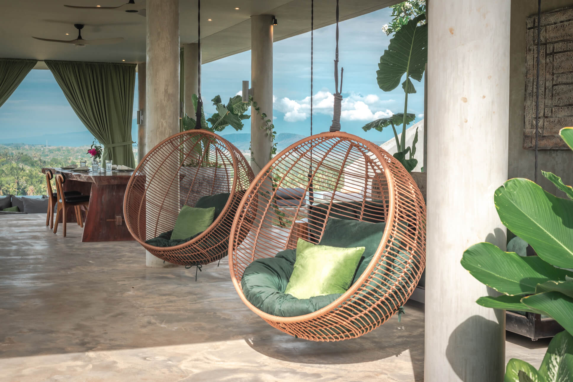 Hanging rattan egg chairs on Villa Simcurik terrace with green cushions, concrete pillars and valley views