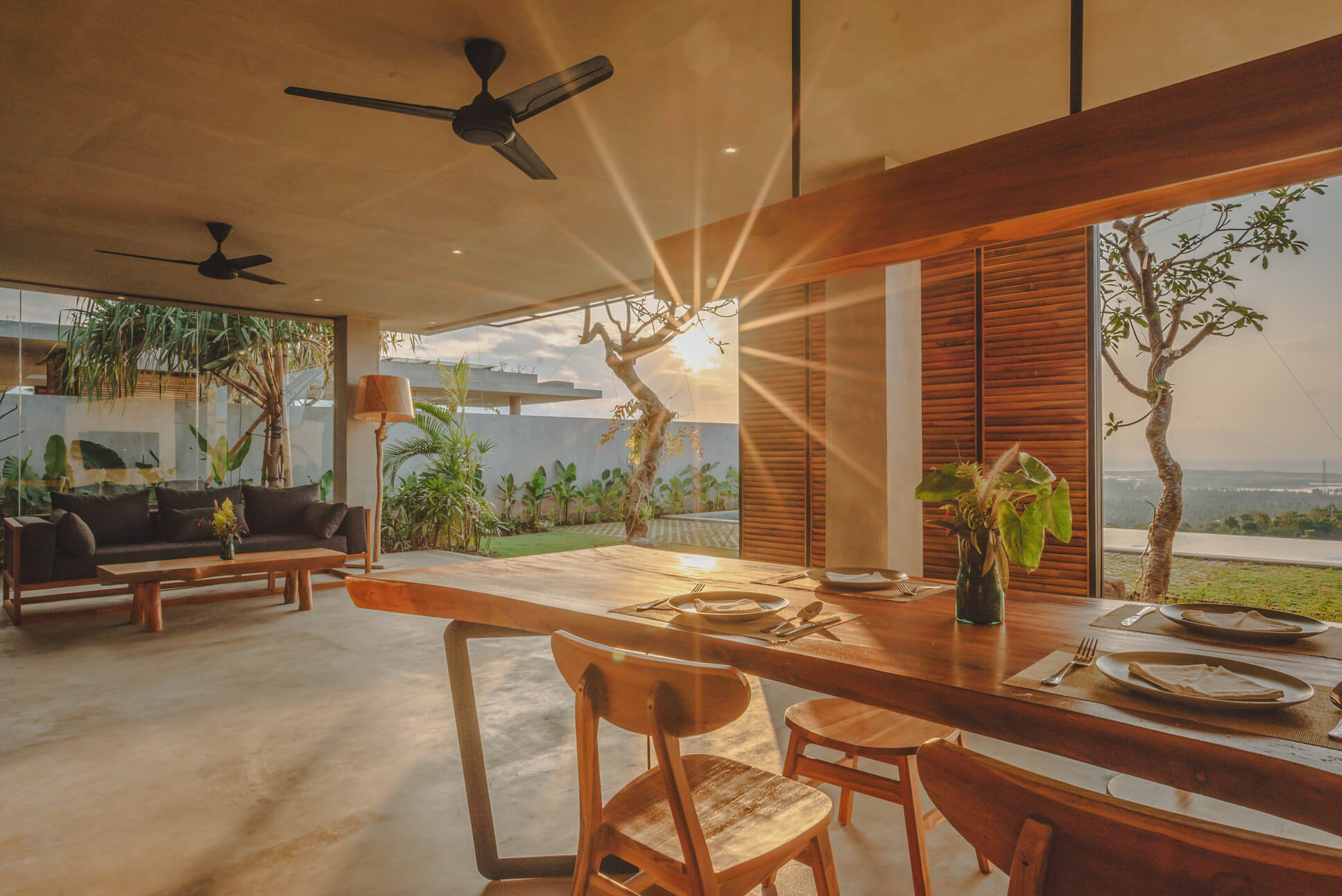 Open-plan dining and living area at Villa Giulia with wooden table, sofa, plants and sunset sea view